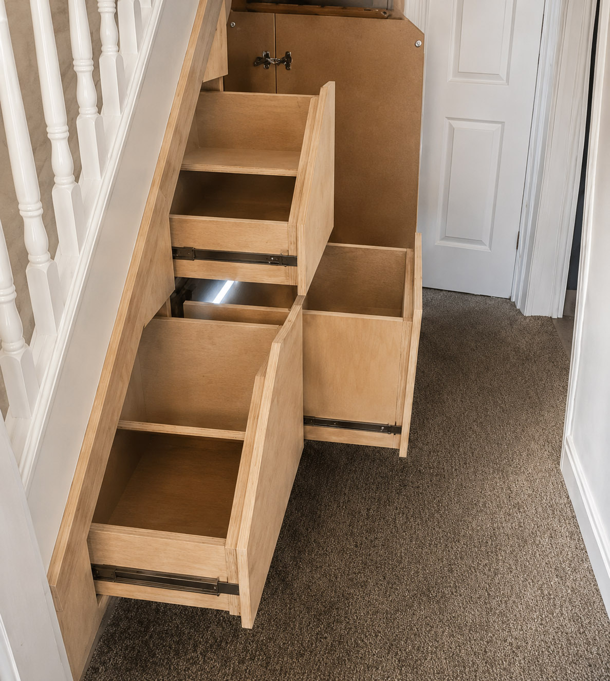 Open bespoke understairs storage by Elite showing deep pull-out drawers and cupboard compartments